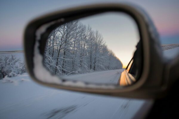 buitenspiegel die terugkijkt op besneeuwde bomen